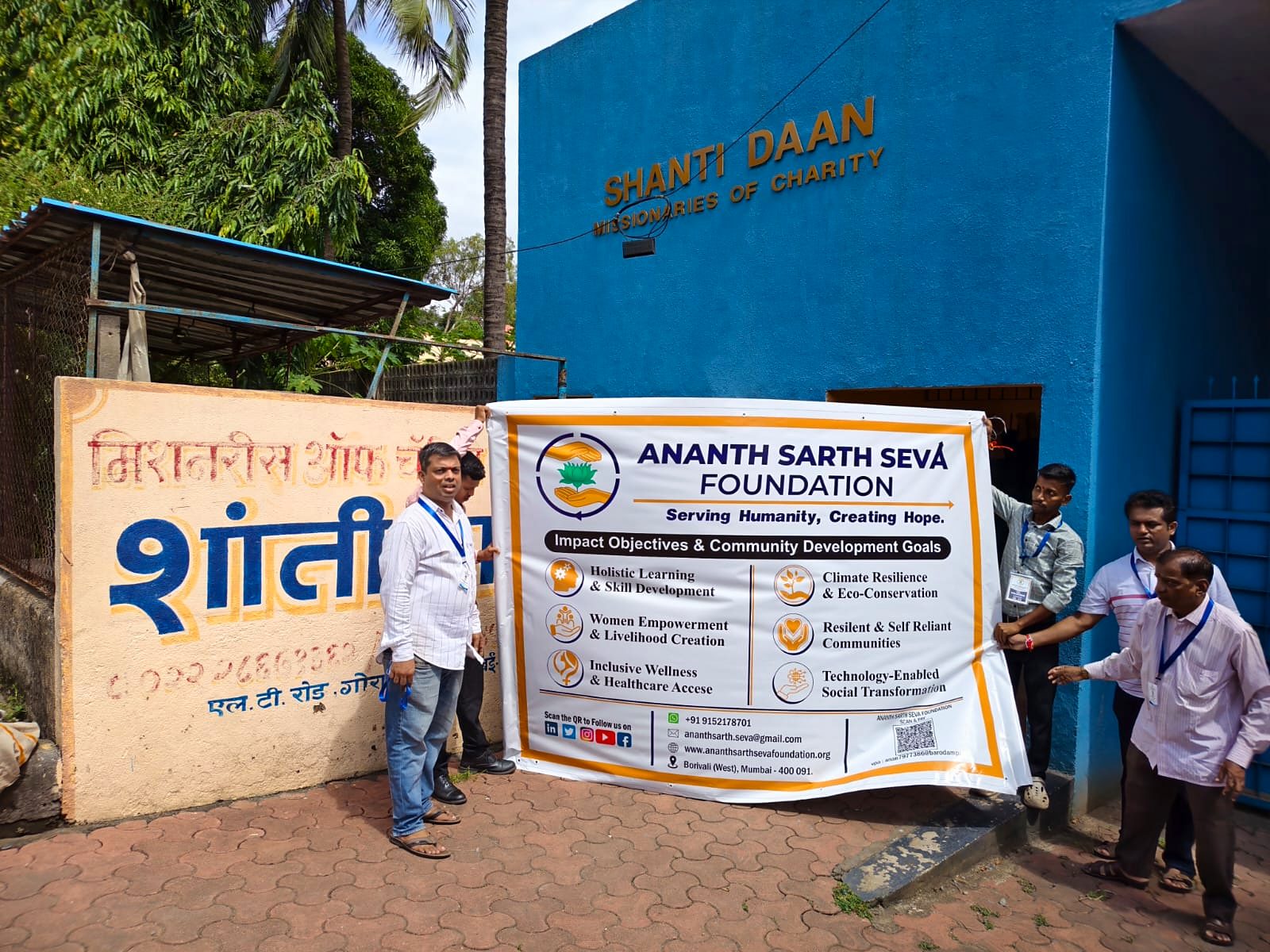 A group holds the foundation banner outside the blue Shanti Daan building.